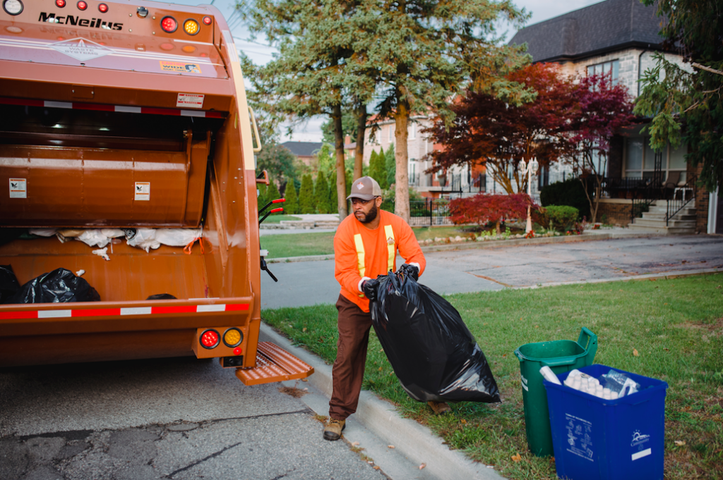 A worker placing a garbage bag into a Miller Waste Systems garbage truck. 
