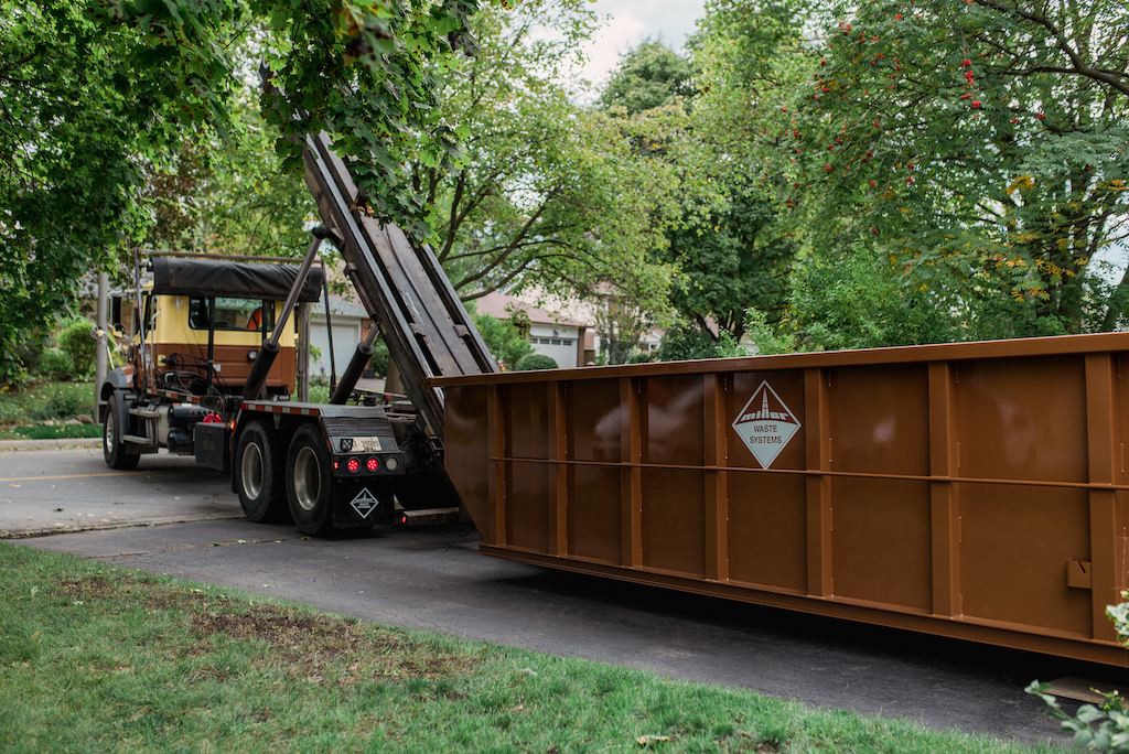 A Miller Waste Systems truck offloading a rental dumpster in a client's driveway.