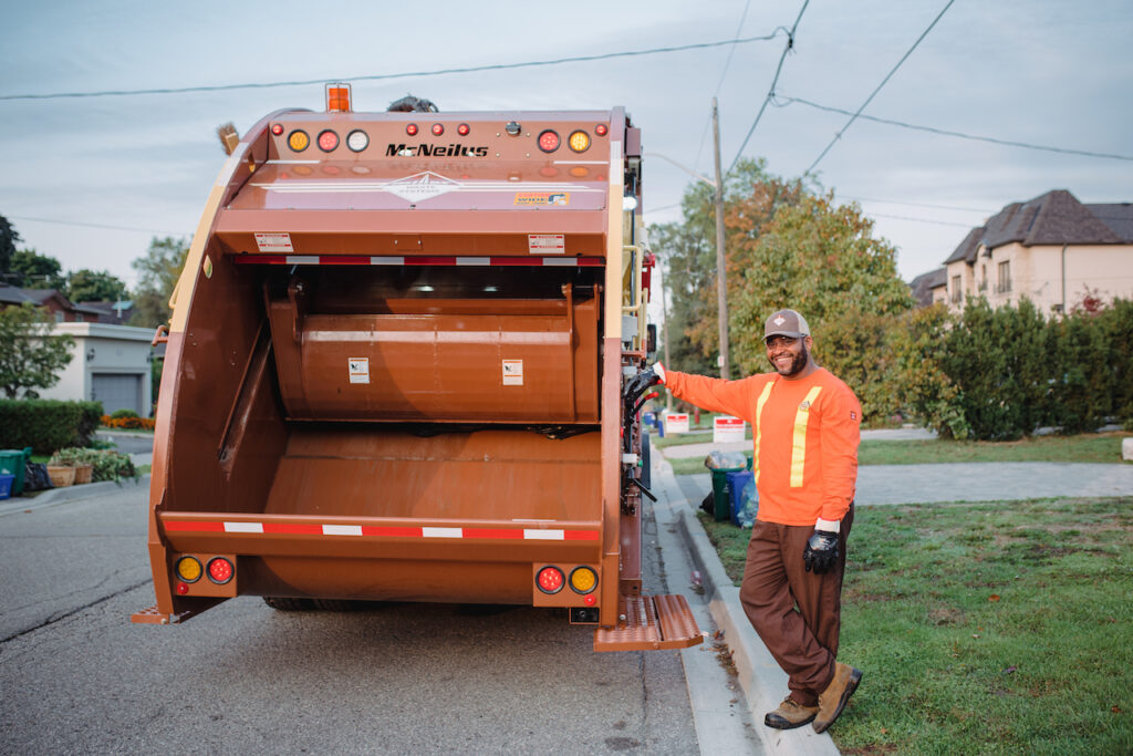 A garbage man beside a Miller Waste waste truck. 