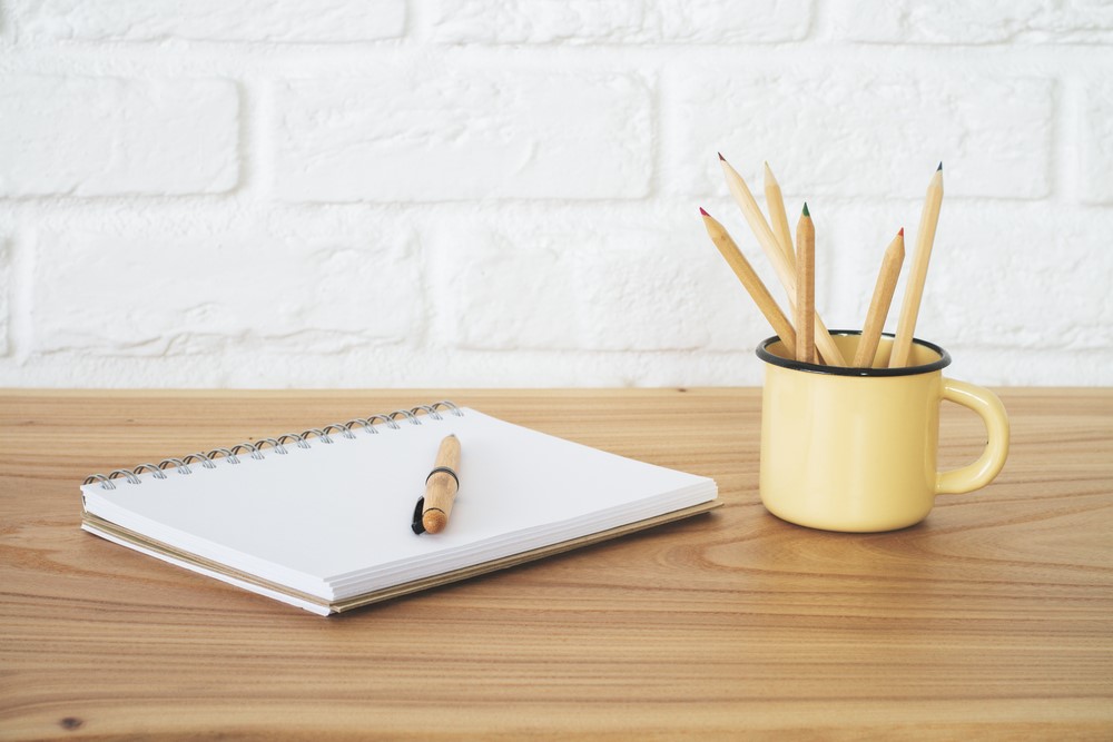 A mug holding pencils beside a notepad and a pen. 