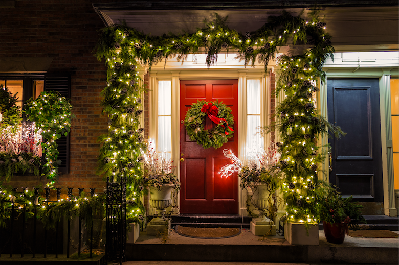 A red front door decorated with garland and Christmas lights.  